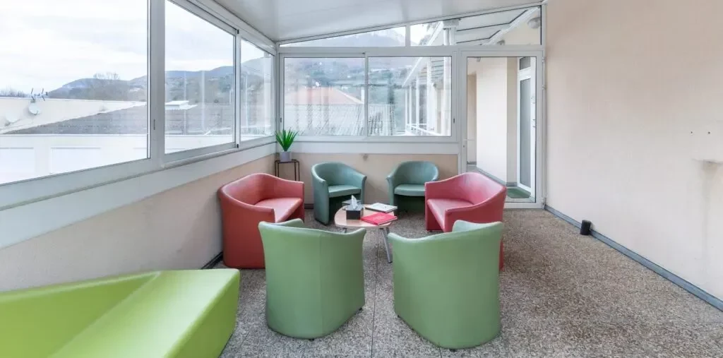 Espace d'attente vitré et lumineux avec des fauteuils colorés pour les proches.