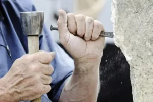 Mains d'un artisan marbrier taillant une pierre avec un burin et un maillet.